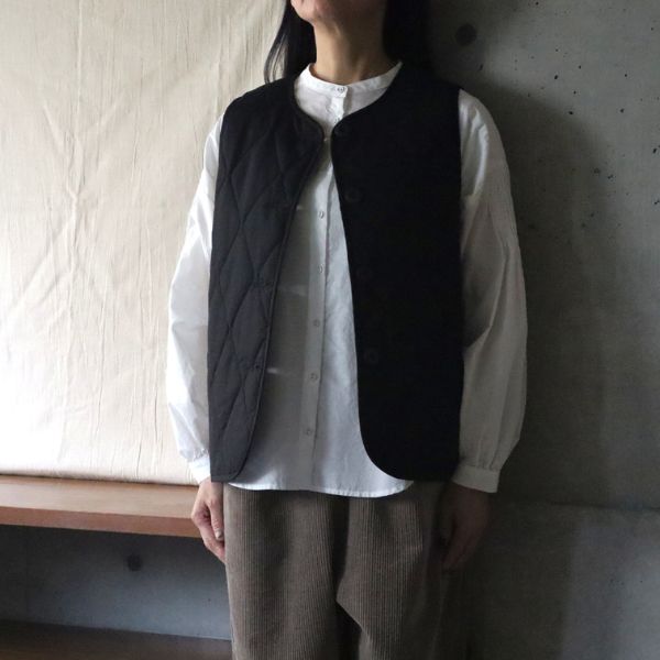 ブラックの中綿入り万能ベストにホワイトシャツを合わせたコーデ。裾のラウンドとスリットが軽やかで、上品な重ね着スタイル。