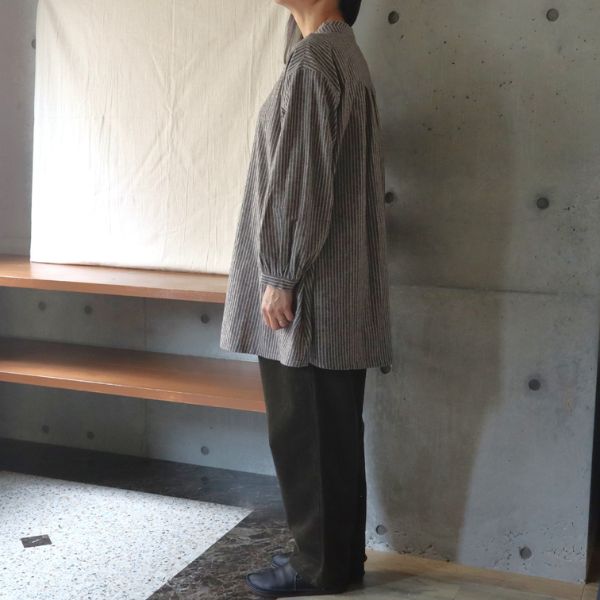 綿麻ストライプチュニックとオリーブグリーンのコーデュロイパンツを着用した女性の全身横向きコーデ写真