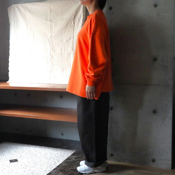 サンセットオレンジのセントラル裏毛ワイドトレーナーとチャコールのカツラギノッポパンツの横向き全身コーデ。裾を絞らずに着たストレートシルエットで、リラックス感のある大人カジュアルスタイルを演出。