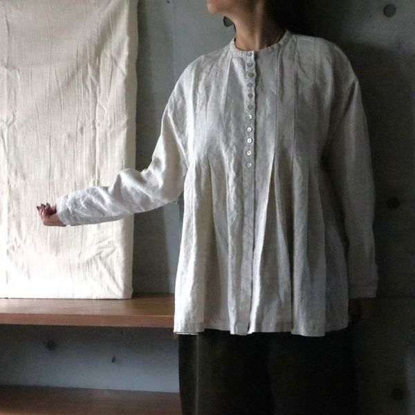 リネンブラウスのピンタックや貝ボタンのディテールを見せる腰上ショット。右手を少し曲げた秋のナチュラルコーデ。