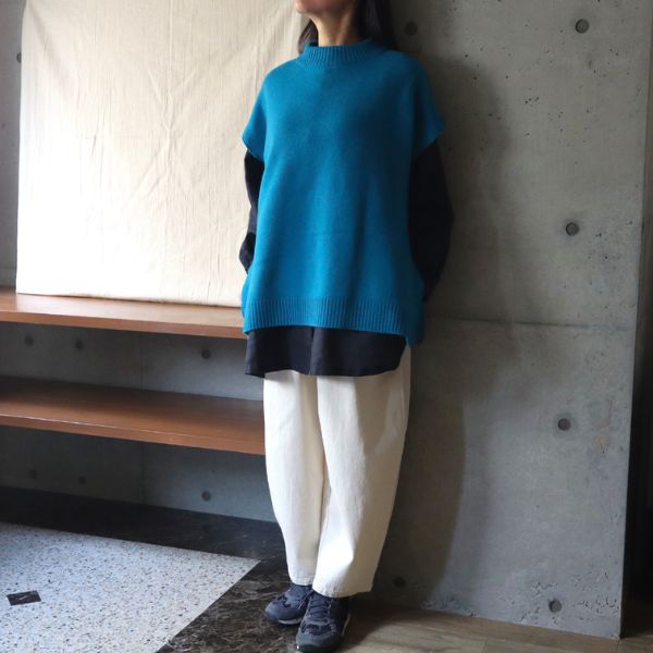 ターコイズ色のウールベストにネイビーのチュニックと白パンツを合わせた全身正面コーデ。軽やかでリラックス感のある大人カジュアルスタイル。