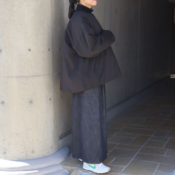 ブラックのノーカラーレギュラーコートに、インディゴのスカート風パンツを合わせた全身コーデ。ノーカラーの首元が美しく、シャーリングで生まれるふんわりしたシルエットが魅力の装い。