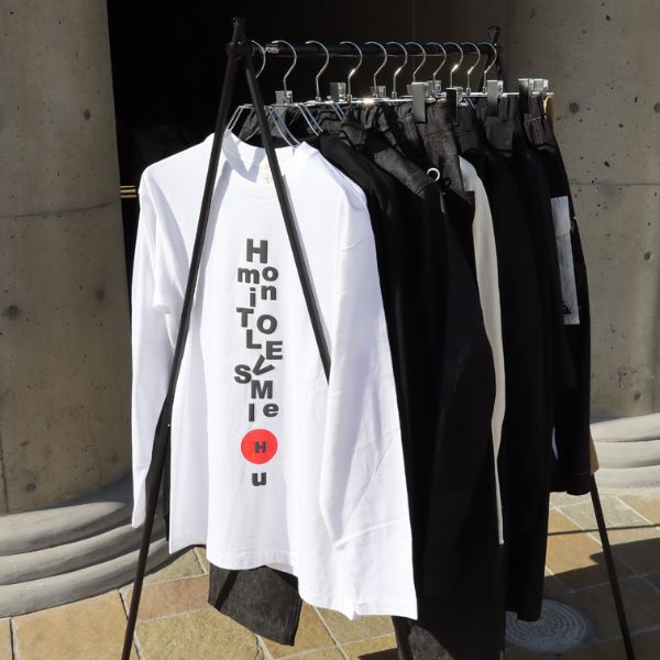 ラックに並ぶエイチマウントのアイテムを屋外で撮影した写真。正面には白い長袖Tシャツがかかり、ブランドらしいミニマルで上質な雰囲気が伝わるディスプレイ。
