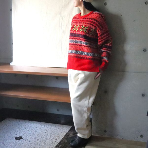 赤地の華やかなフェアアイルニットにキナリの裏起毛コージーパンツを合わせた斜め全身写真。鮮やかな柄が顔まわりを明るく見せる、冬らしいあたたかみのある大人可愛いコーデ。