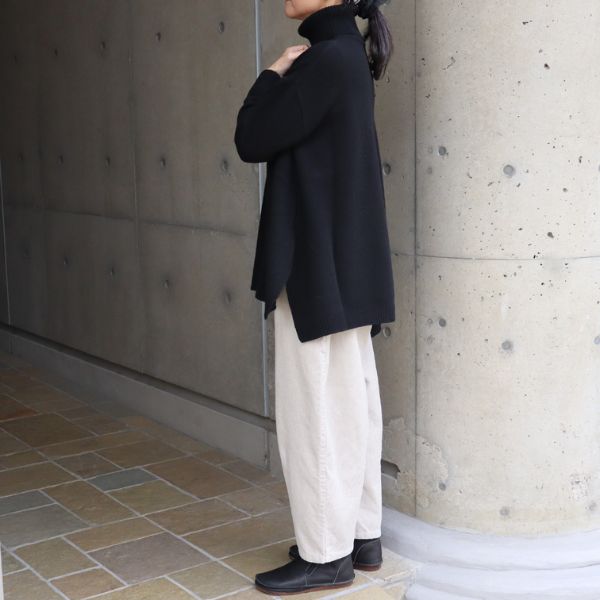 黒のアラスカタートルニットの前後差シルエットが見える横向き写真。白系コーデュロイエッグパンツと合わせたクリーンな冬コーデ。