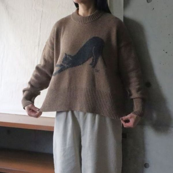 伸び猫コモドニットのウエストショット。裾を少し広げて、フロントに大きく描かれた“のびをする猫”のイラストをしっかり見せた1枚。