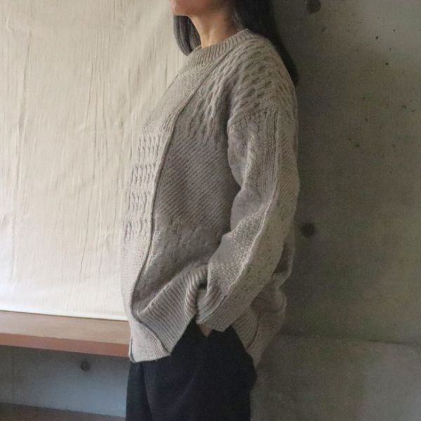 杢ベージュのNATURAL COLORED WOOL柄編みニットを着用した女性の腰上横向き写真。自然色羊毛の深みと立体感ある編み柄が引き立つ、上品であたたかい冬の大人ニット。