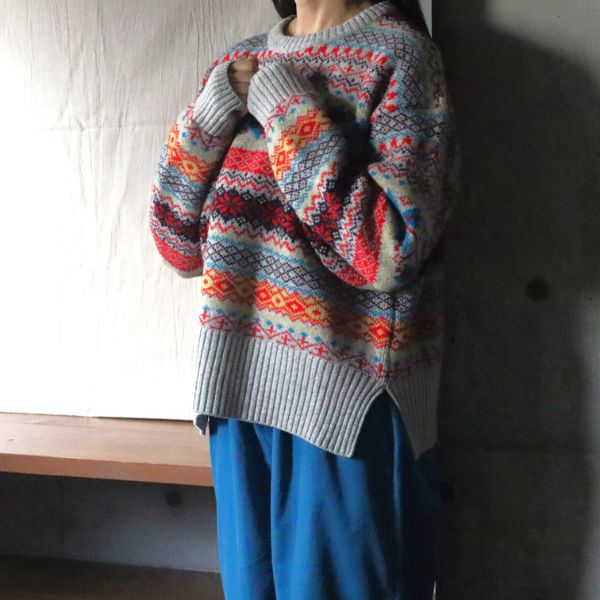 グレーのタスマニアラムフェアアイルニットにスチールブルーのシャツコールコージーパンツを合わせた冬コーデ。胸元で腕を重ね、袖口の繊細なリブと柄の美しさが引き立つ上品な大人のナチュラルスタイル。