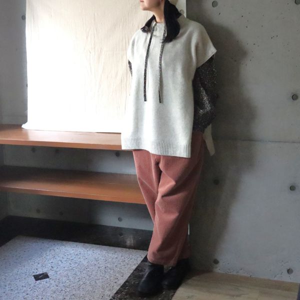 白いニットベストに小花柄ブラウスを重ね、ピンクのコーデュロイパンツを合わせた女性の正面全身写真。楽ちんなのにきちんと見える大人のカジュアルコーデ。