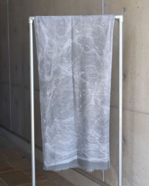 グレーカラーのウール×真綿ニードルパンチストールをラックにかけた商品写真。繊細な柄と素材の重なりが際立つ。