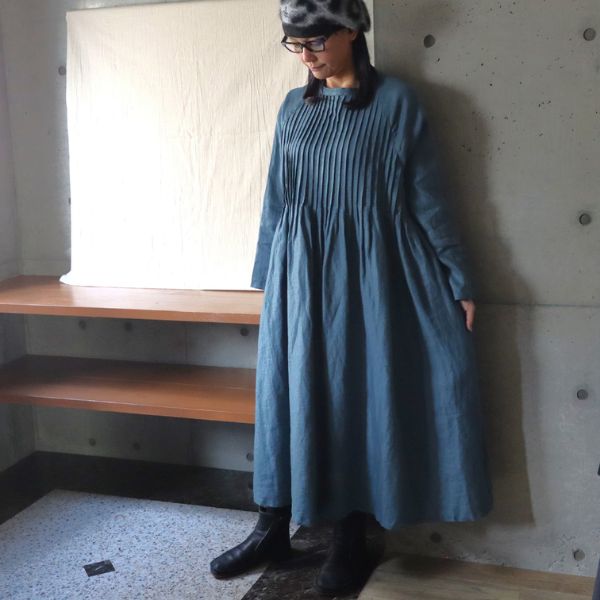 ダルブルー色のピンタック入りラグラン袖ワンピースを一枚でさらりと着た女性の正面全身写真。リネン素材の自然な風合いが映える大人ナチュラルスタイル。