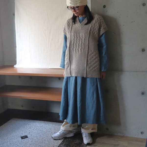 ピンタックワンピースにオートミール色の柄編みウールベストを重ね、内側にキナリのパンツを合わせた女性の正面全身写真。重ね着でスカートのように見せた冬の着回しコーデ。