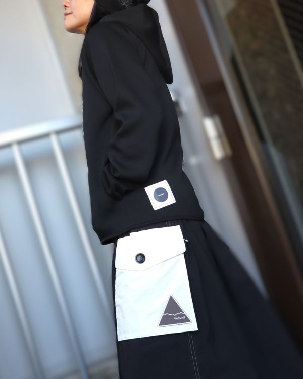 エイチマウント、ダンボールニットパーカー。フードとコーデュラ配色パッチポケットスカートのディテールが見える横向きの女性着用写真。