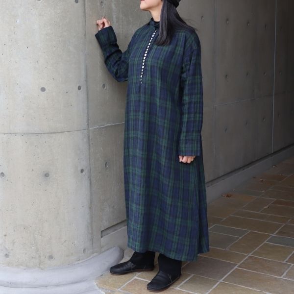ブラックウォッチの多ボタン衿付きワンピースに、ブラックのシャツコールコージーパンツを合わせた全身正面コーデ。緑系チェックのやさしい表情とAラインシルエットが、ふんわりナチュラルな大人の重ね着スタイルを演出。
