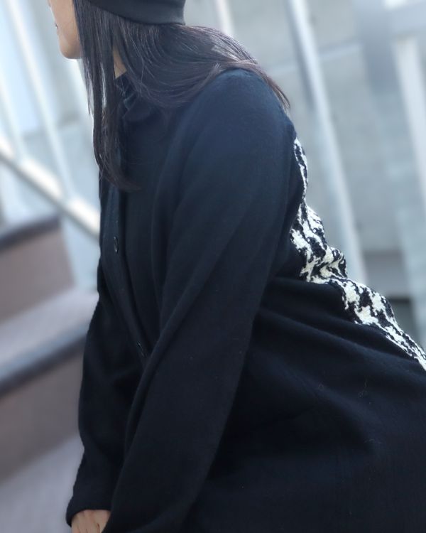 エイチマウント、ウィメンズ ウールジャケット ブラック。横向きに座った着用写真 袖と背中に施された千鳥柄が見えるデザイン。