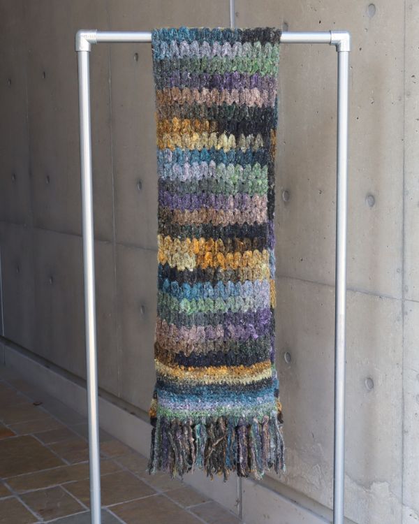 NORO Yarnの手編みマフラーをラックにかけた商品写真。天然素材ならではの個性的な表情とユニセックスなデザインが魅力。