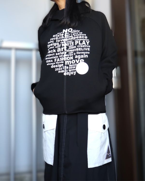 エイチマウント、ダンボールニットパーカー ブラック。女性着用。フロントロゴとコーデュラ配色パッチポケットスカートの正面ディテールがわかる写真。