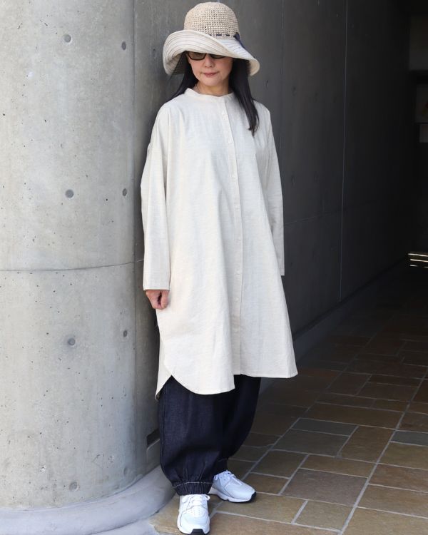 コットンリネン素材のバンド襟リネンチュニック(キナリ)と、インディゴカラーの裾ゴム入りポップパンツを合わせたナチュラル大人女性の全身コーディネート正面写真。膝が隠れる長め丈チュニックで体型をやさしくカバー。