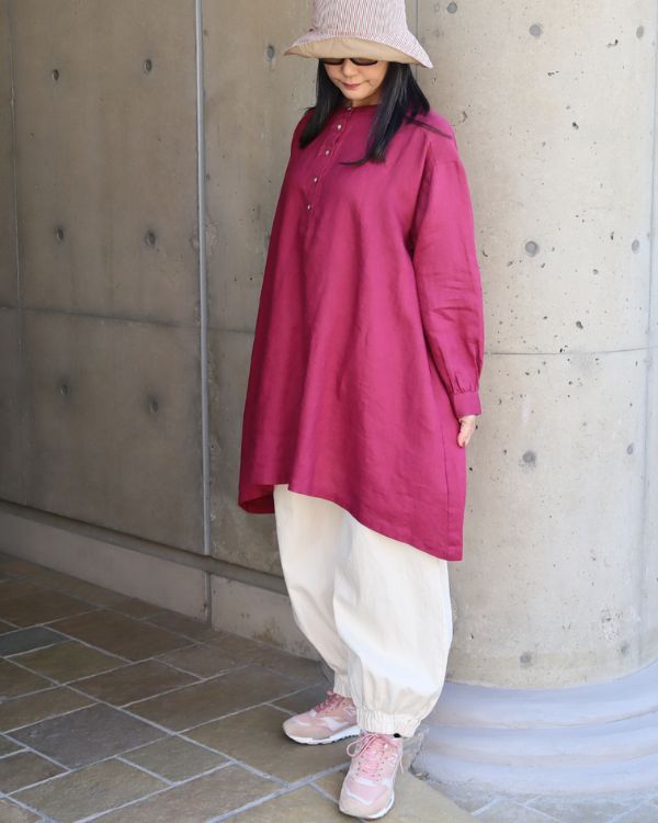 ワインレッドのボリューム袖ヘンリーあきチュニックと、キナリ色の裾ゴム入りポップパンツを合わせたナチュラル大人女性の全身正面コーデ。ひざ丈のゆったりシルエットが落ち着いた雰囲気。