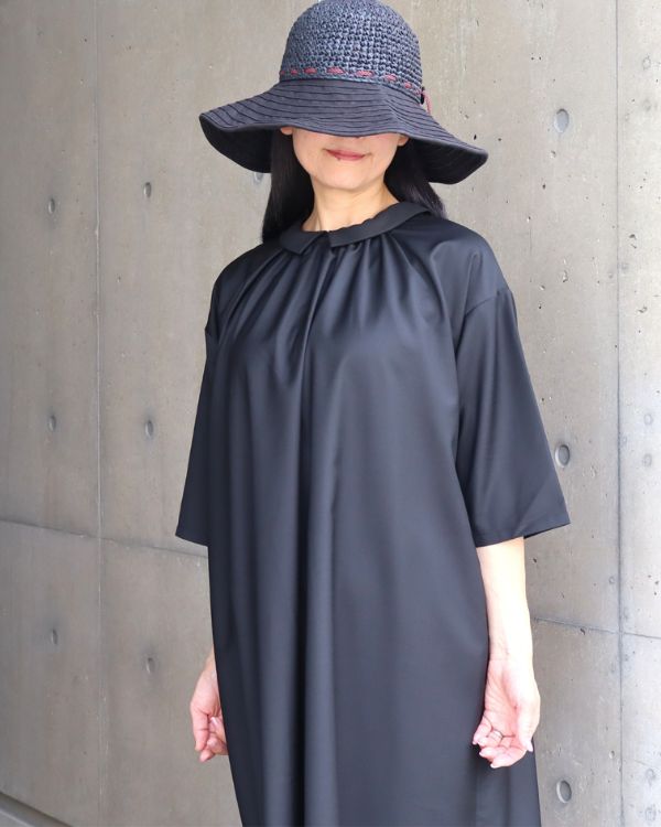 名古屋・覚王山のセレクトショップ コッピアーナでご紹介する、一枚で品よく決まる2way襟付きワンピースのギャザー側を前に着用した上半身写真です。光沢感のあるブラックの上質な素材と、襟元のやわらかなギャザーが美しい表情を演出し、オケージョンから普段のお出掛けまで幅広く活躍します。