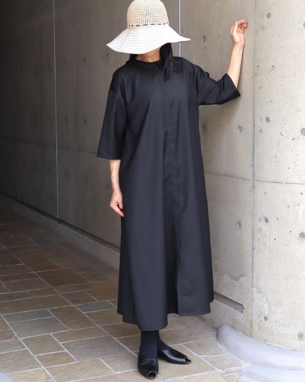 名古屋・覚王山のセレクトショップ コッピアーナでご紹介する、ブラックの2way襟付きワンピースを比翼仕立て側を前に着用した全身写真です。裾を軽く持ち上げた自然な動きが、光沢感のある素材の美しさと軽やかなシルエットを引き立てています。