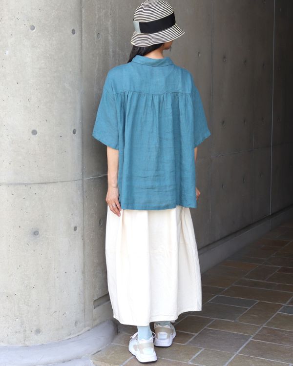 リネンシャンブレーシャツ衿ピンタックブラウスのターコイズを後ろ姿から撮影した全身イメージ。リネンシャンブレー素材のやわらかなシルエットと爽やかな色合いが伝わり、名古屋・覚王山のセレクトショップ コッピアーナがおすすめする、夏の街歩きや休日のお出かけにぴったりのコーディネートです。