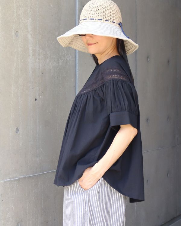 ハシゴレース切替ブラウス（ブラック）の横向き着用イメージ。ふんわりとしたギャザーシルエットが自然な体型カバーを叶え、やわらかなコットン素材で暑い季節も快適に過ごせる店頭限定ブラウスです。