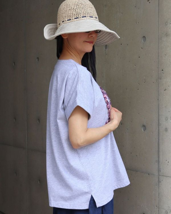 コットンジャージーチェックフリル半袖Tシャツのグレーを横向きで撮影した上半身の着用イメージ。ロールアップ風の袖と裾にさりげなく入ったスリットが見え、シンプルなTシャツスタイルに細やかなデザインの工夫が感じられます。