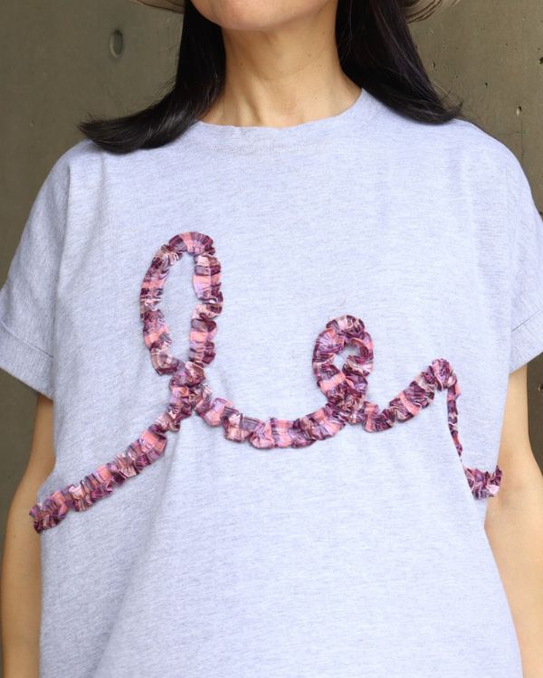 コットンジャージーチェックフリル半袖Tシャツの前見頃に施されたチェック柄の立体フリルをアップで撮影した写真。グレーの落ち着いた色合いに表情豊かなフリルが映え、コットン100％のやわらかな素材感も伝わります。