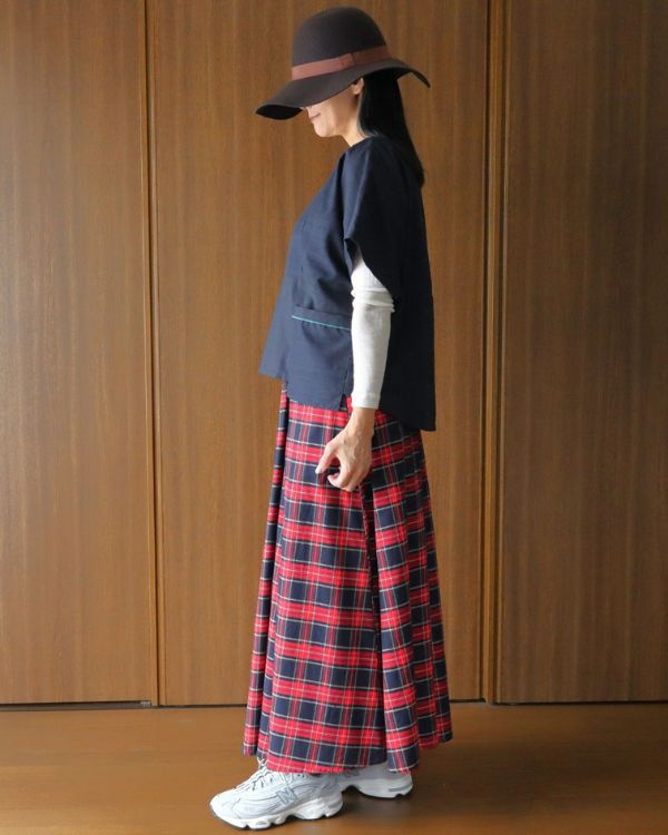 名古屋・覚王山のコッピアーナで紹介する、紺シルクシンプルトップスとロイヤルタータン タックロングスカートの横向き着用写真。アイボリーのウールリブロングスリーブを重ね、タータンチェックの秋らしさを楽しむ装いです。