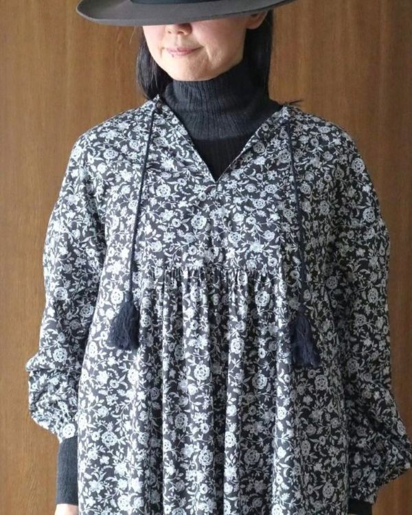 名古屋・覚王山のコッピアーナで取り扱う、綿100%のフラワープリントキーネックワンピースの首元と生地を写した写真です。ブラック地の落ち着いた小花柄とタッセル付きの紐が印象的です。