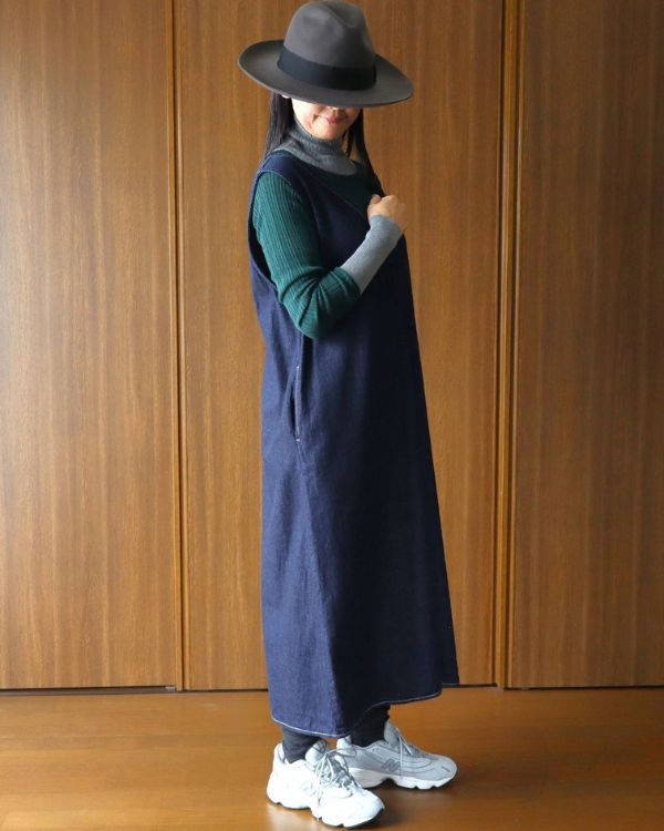 名古屋・覚王山のセレクトショップ コッピアーナで紹介する、インディゴの8オンスムラデニムジャンパースカートを斜め前から着用した写真。深いVネックでシャツやニットとのレイヤードを楽しめる着用イメージです。